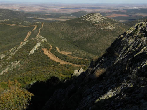 Desde los aledaños de la cumbre, el camino gira y desciende bruscamente hacia el nordeste, paralelo a la valla. Unos metros más abajo, se ciñe a unos llamativos escarpes y los sortea por la derecha. Continúa después más o menos paralelo al que utilizamos para subir, sólo que a más altura, lo que nos permite ir disfrutando de unas hermosas vistas sobre el valle, la colonia de Cinco Casas y la Loma de los Carros.